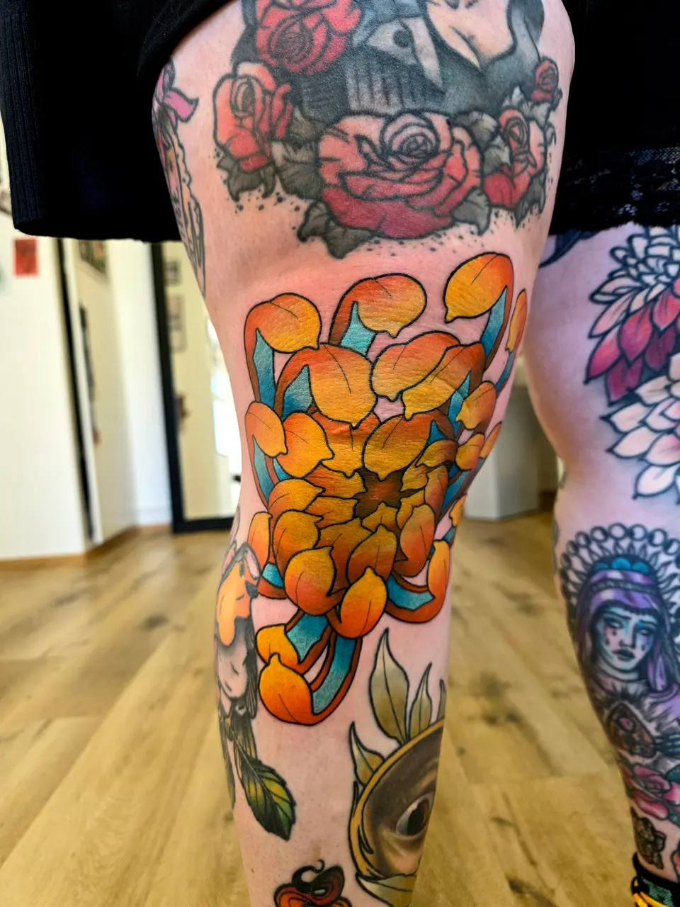 Chrysanthème orange tatoué en couleur sur un genou
