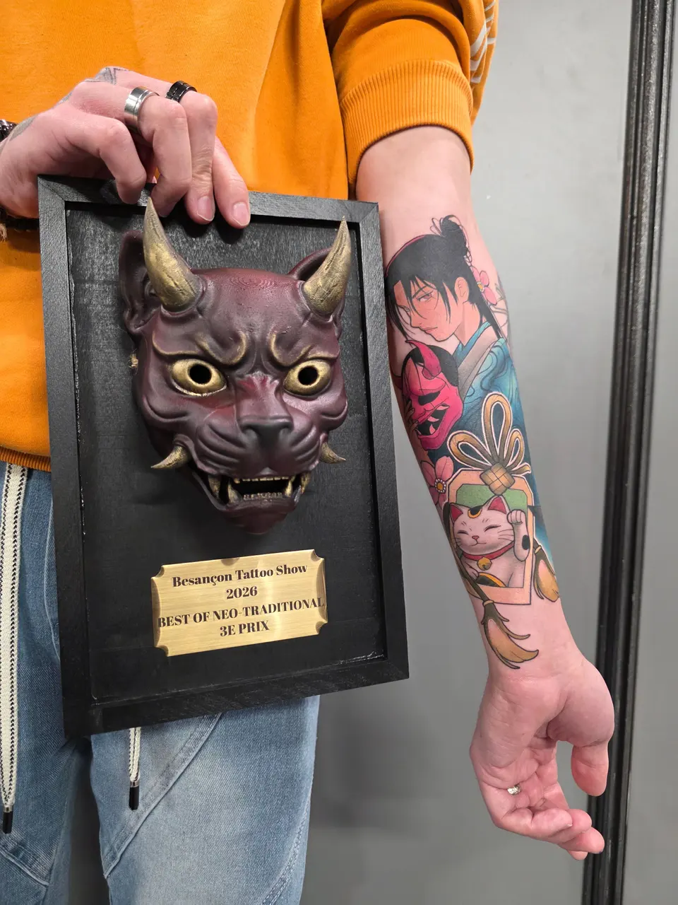 Récompense en forme de masque présentée à côté de l'avant-bras tatoué