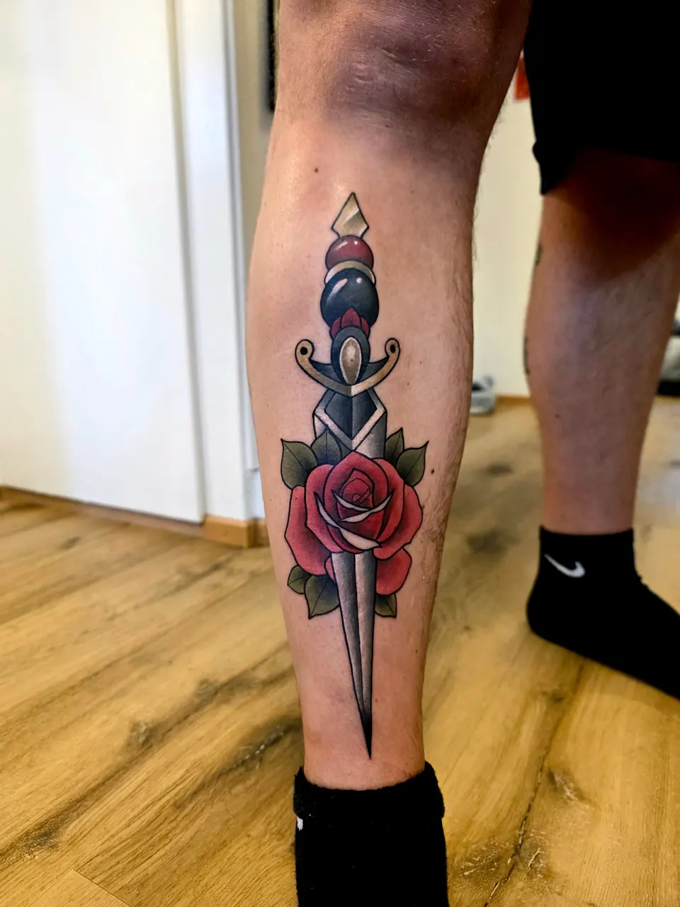 Dague et rose rouge, tatouées sur le mollet