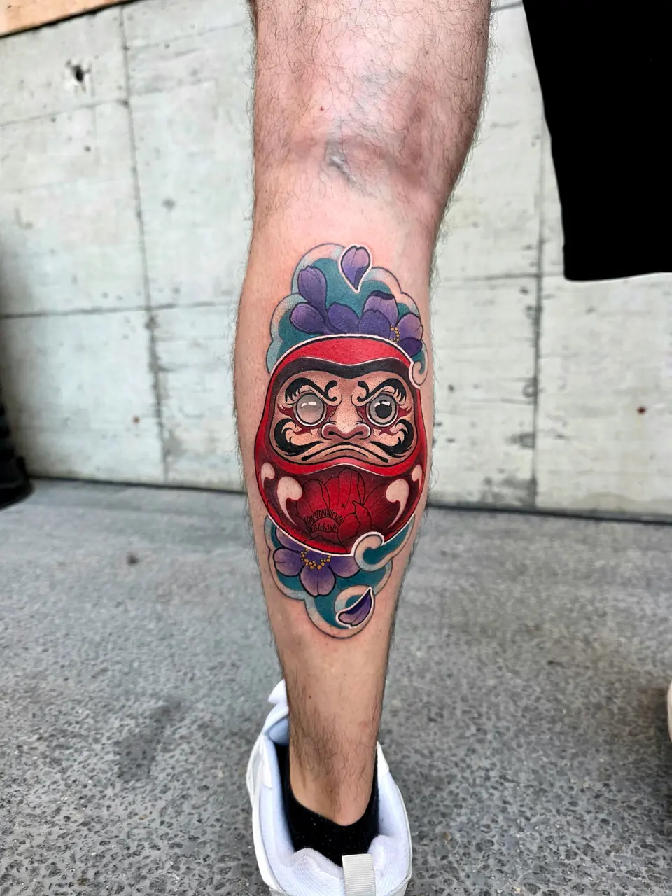 Daruma rouge coiffé d'une fleur violette, sur le mollet