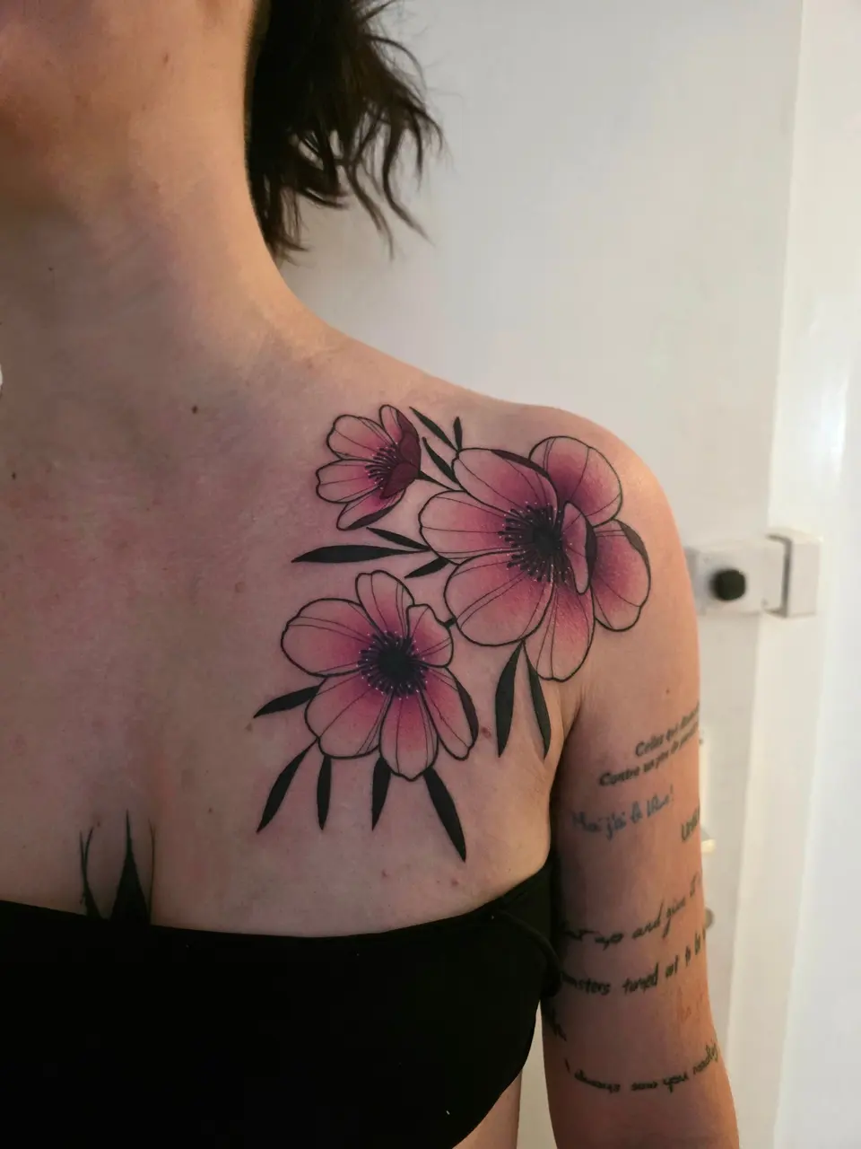 Fleurs aux pétales colorés et feuillage tatoués sur l'épaule