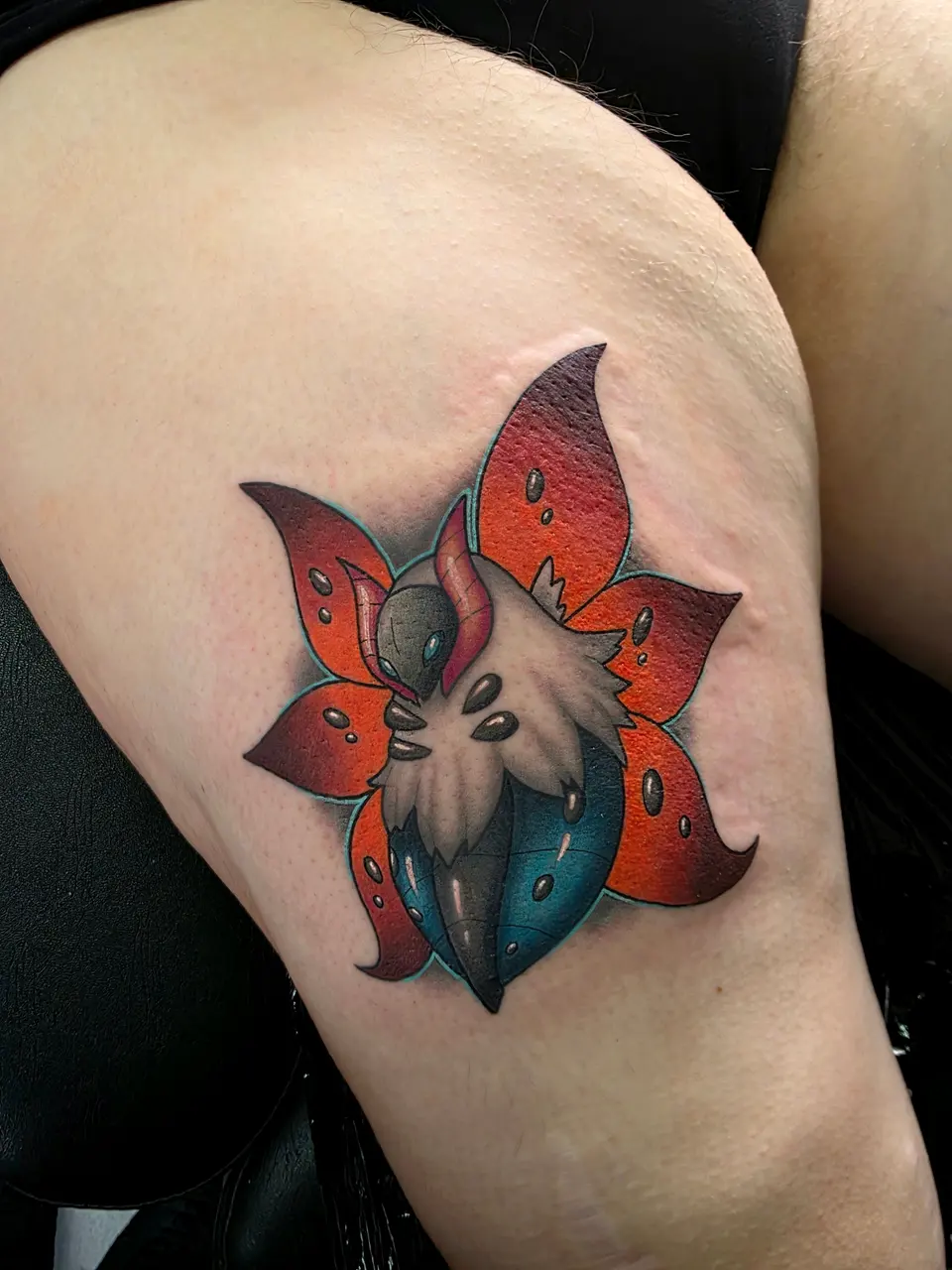 Tête d'oiseau au cœur d'une fleur rouge et orange, sur la cuisse