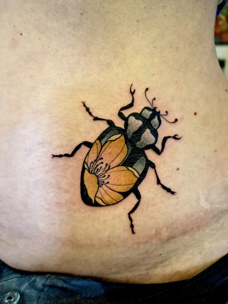 Scarabée noir aux ailes jaunes, tatoué sur la hanche
