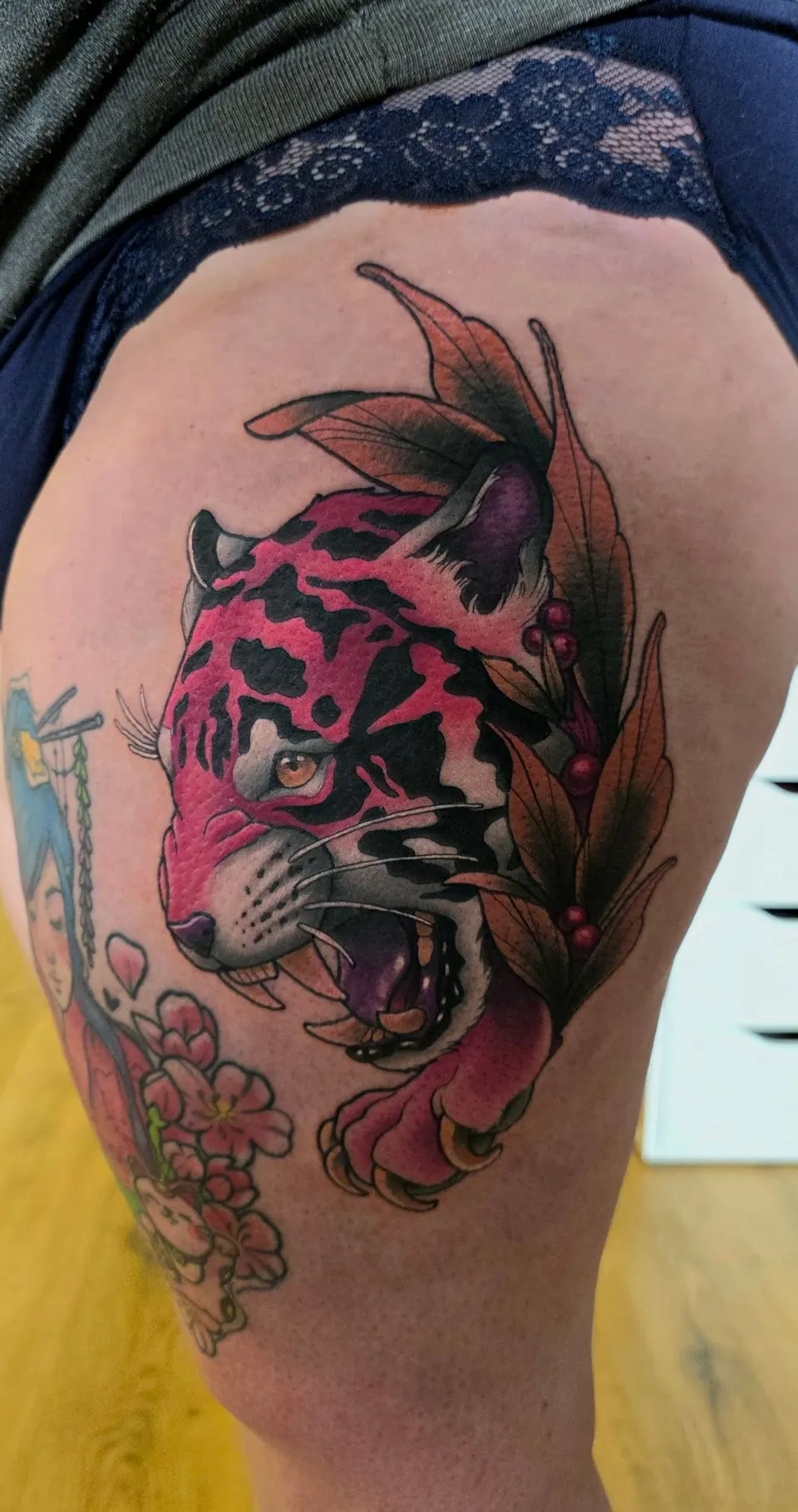 Tigre rugissant entouré de fleurs, tatoué sur la cuisse